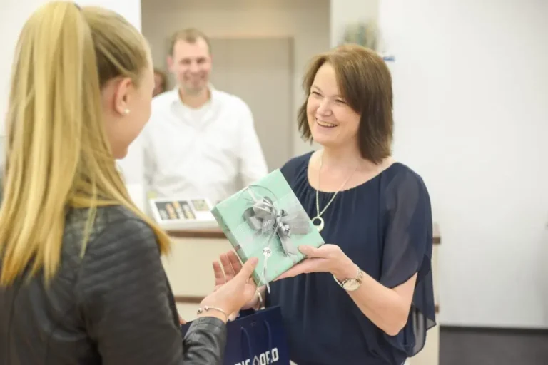 Erstklassiger Service bei Meyer & Rademacher: Eine Mitarbeiterin überreicht nach einer persönlichen Beratung ein elegant als Geschenk verpacktes Schmuckstück im Geschäft.